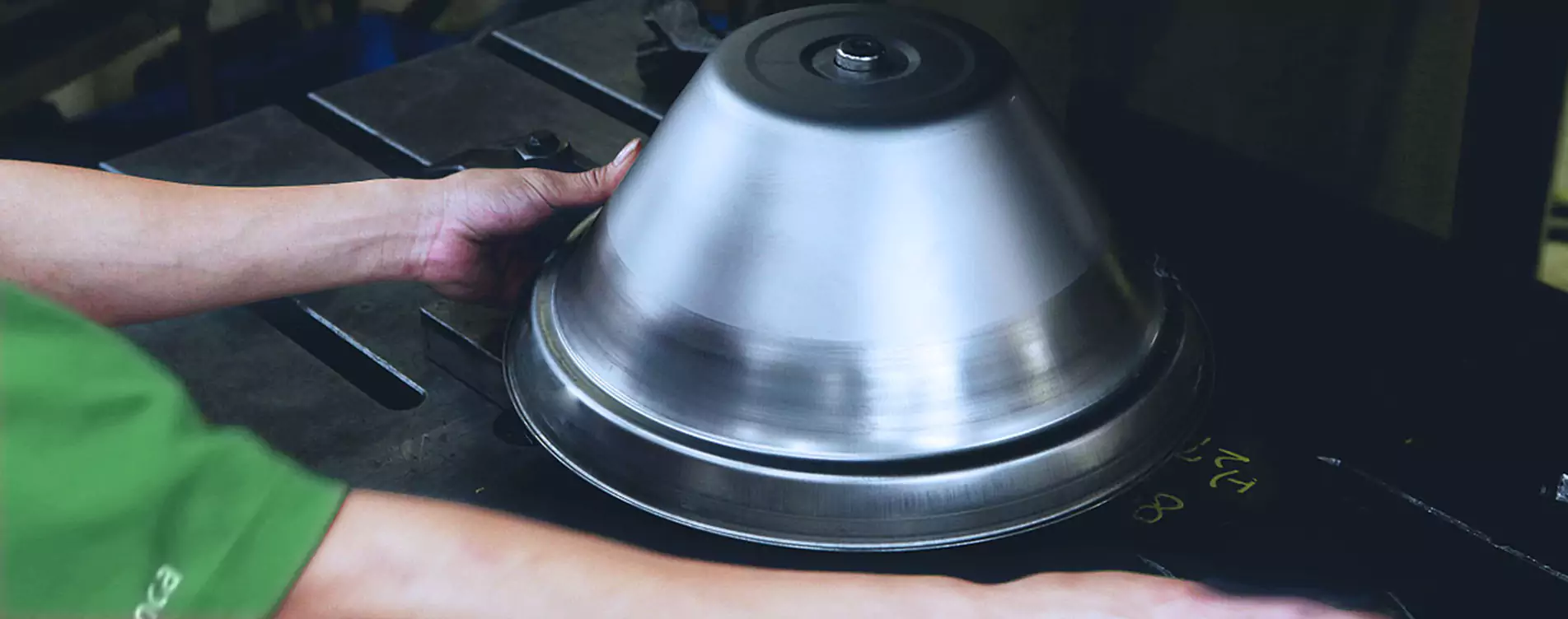 YBT operator handling a spun stainless steel patio heater reflector on a forming press